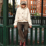 Person in the cream corduroy jacket and a cap sitting on a green railing in a London square
