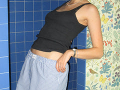 Blue and white striped unisex boxer shorts paired with black tank top, styled against blue tiles and floral wallpaper.