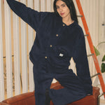 Woman in the navy corduroy jacket and matching trousers, one arm raised, sitting on an orange chair
