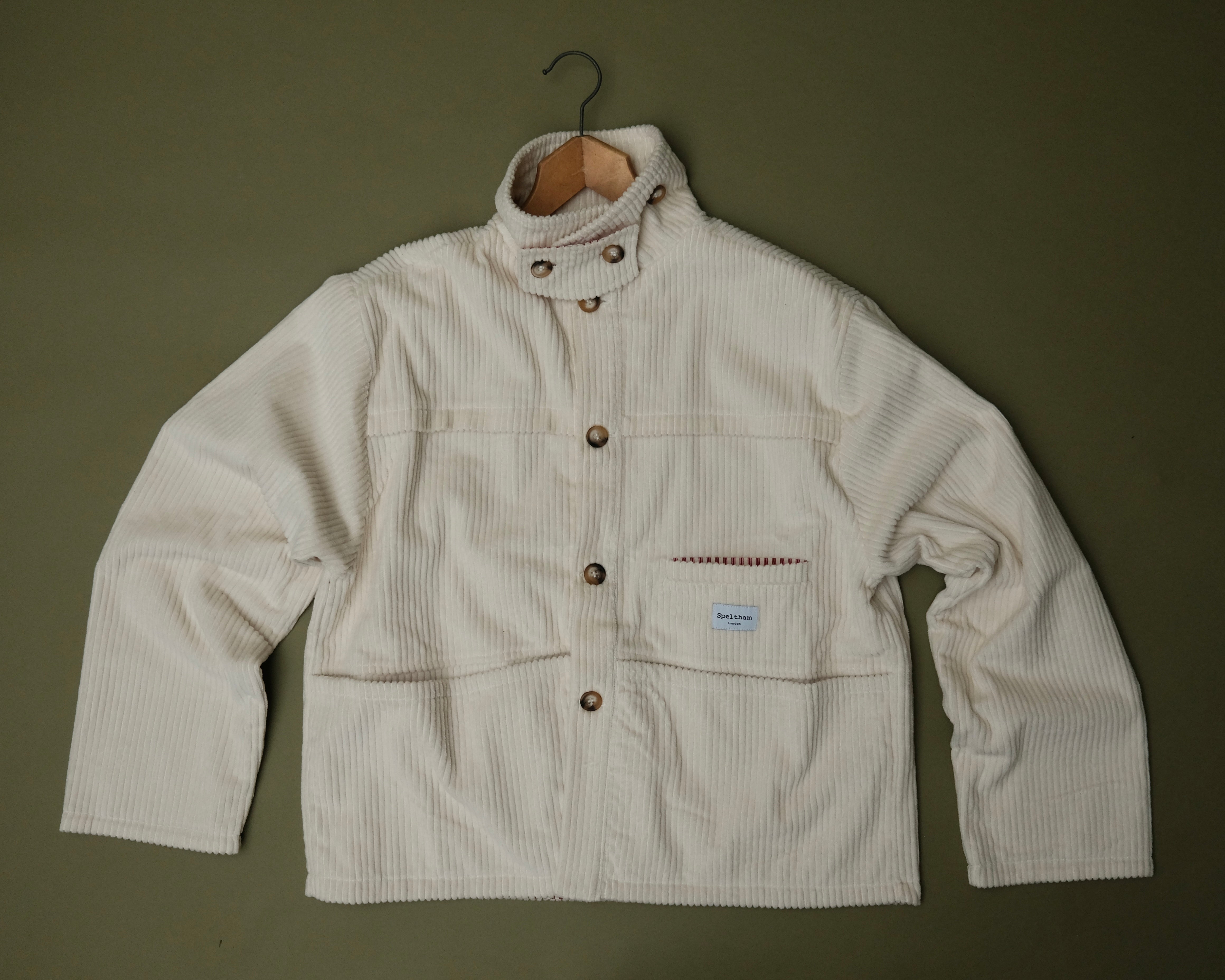 Speltham cream corduroy jacket on a hanger against a sage green wall, showing the button front and patch pockets