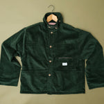 Speltham green corduroy jacket on a hanger against a sage green wall, showing the button front and patch pockets