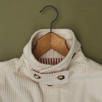 Close-up of the cream corduroy jacket collar on a wooden hanger, showing the striped lining and buttons