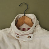 Close-up of the cream corduroy jacket collar on a wooden hanger, showing the striped lining and buttons