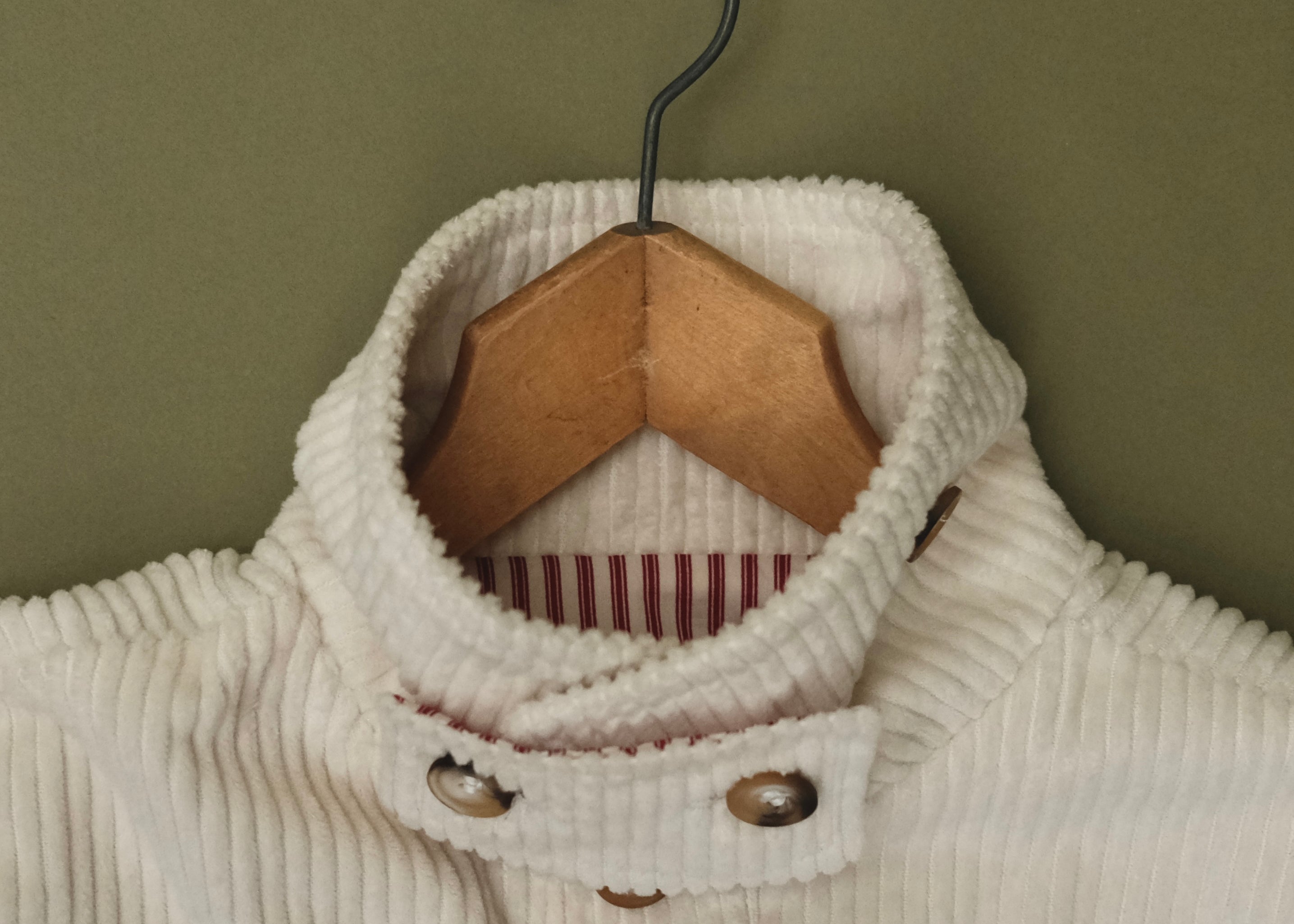 Close-up of the cream corduroy jacket collar on a wooden hanger, showing the striped lining and buttons