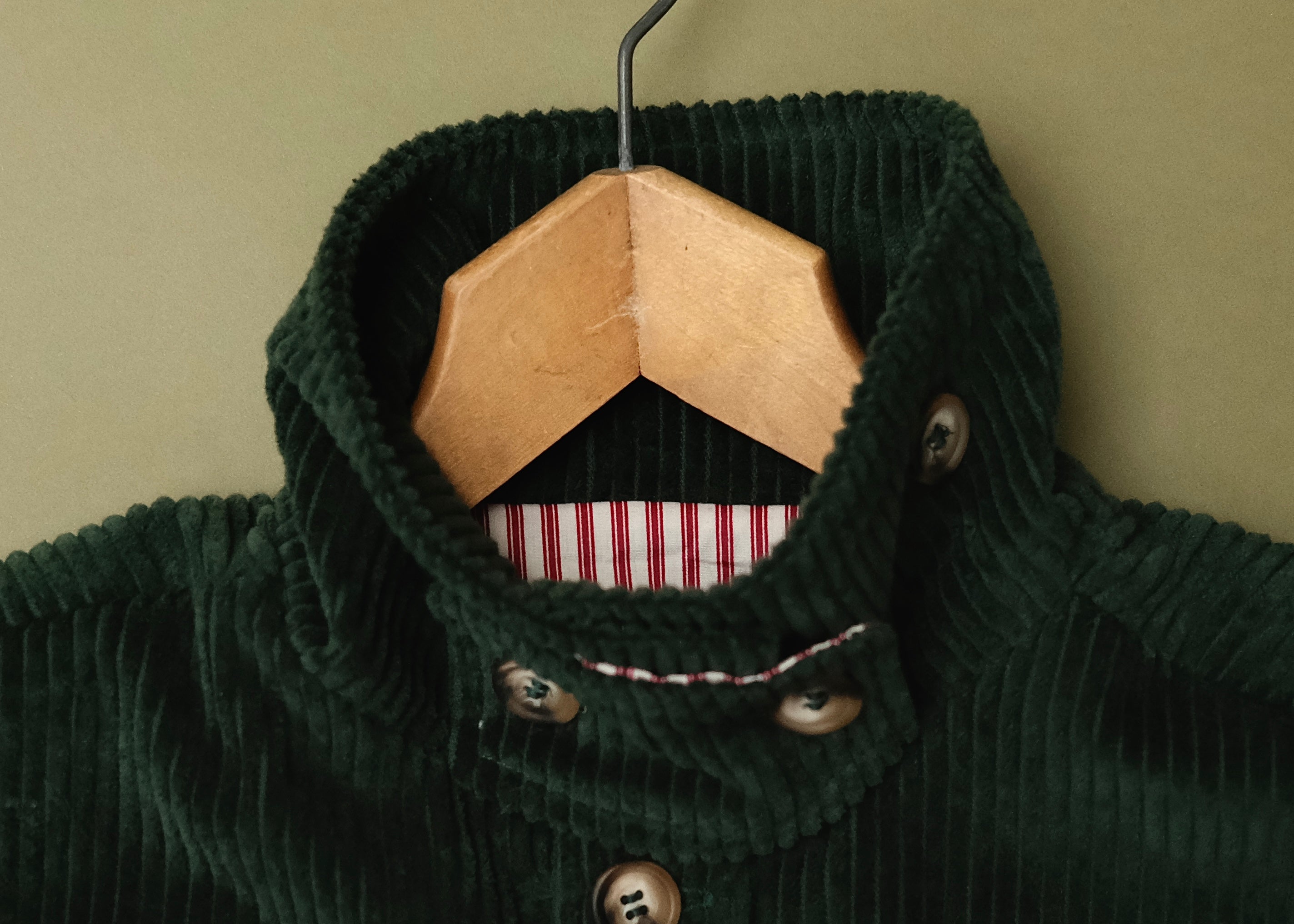 Close-up of the green corduroy jacket collar on a wooden hanger, showing the wide wale cord and striped lining