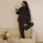 Woman in the brown corduroy jacket and matching trousers leaning against a wall, cuffs turned back to show the striped lining