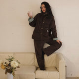 Woman in the brown corduroy jacket and matching trousers leaning against a wall, cuffs turned back to show the striped lining
