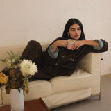Woman relaxing on a sofa with a mug, wearing the brown corduroy jacket with cuffs rolled to show the Speltham stripe lining